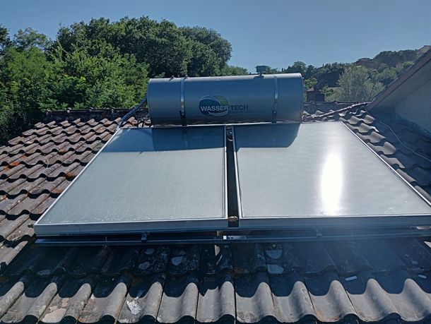 Pannelli solari per il riscaldamento dell'acqua su un tetto di tegole, sotto un cielo azzurro e limpido.