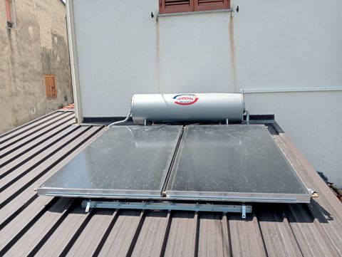 Pannelli solari per il riscaldamento dell'acqua installati su un tetto accanto a una parete bianca.