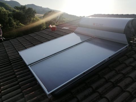 Pannelli solari per il riscaldamento dell'acqua su un tetto di tegole all'alba, con le montagne sullo sfondo.