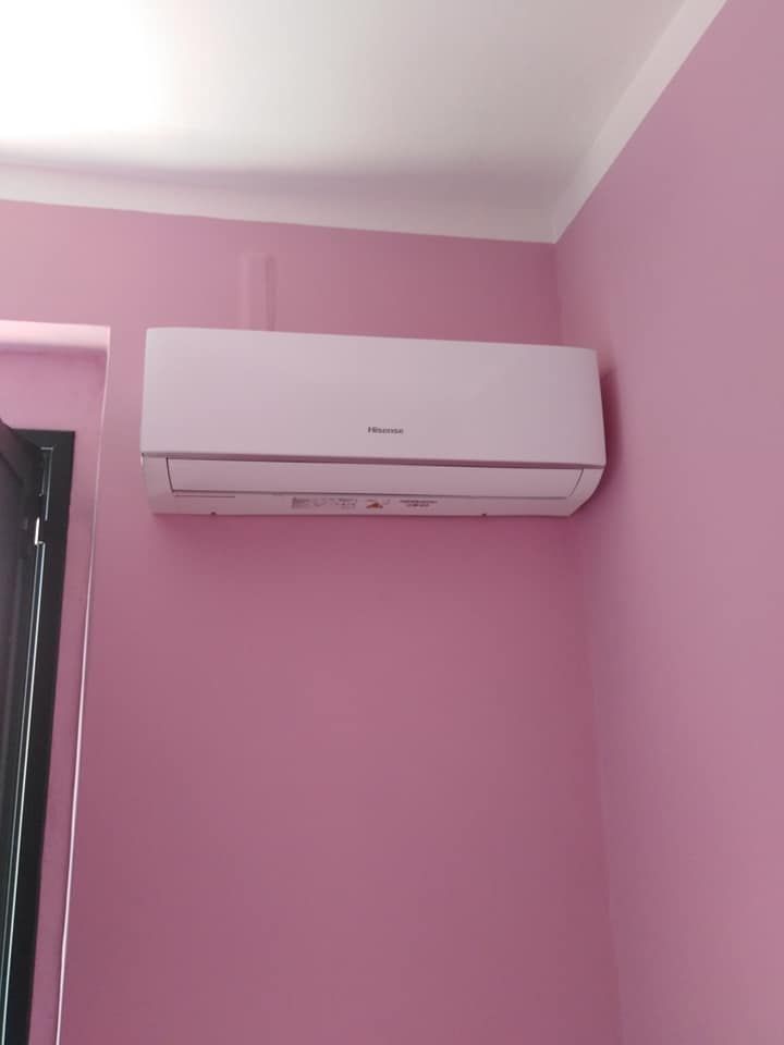 Condizionatore d'aria bianco a parete, installato su una parete rosa della camera da letto, vicino al soffitto.