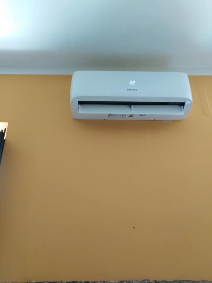 Condizionatore d'aria bianco a parete, installato su una parete color beige vicino al soffitto.