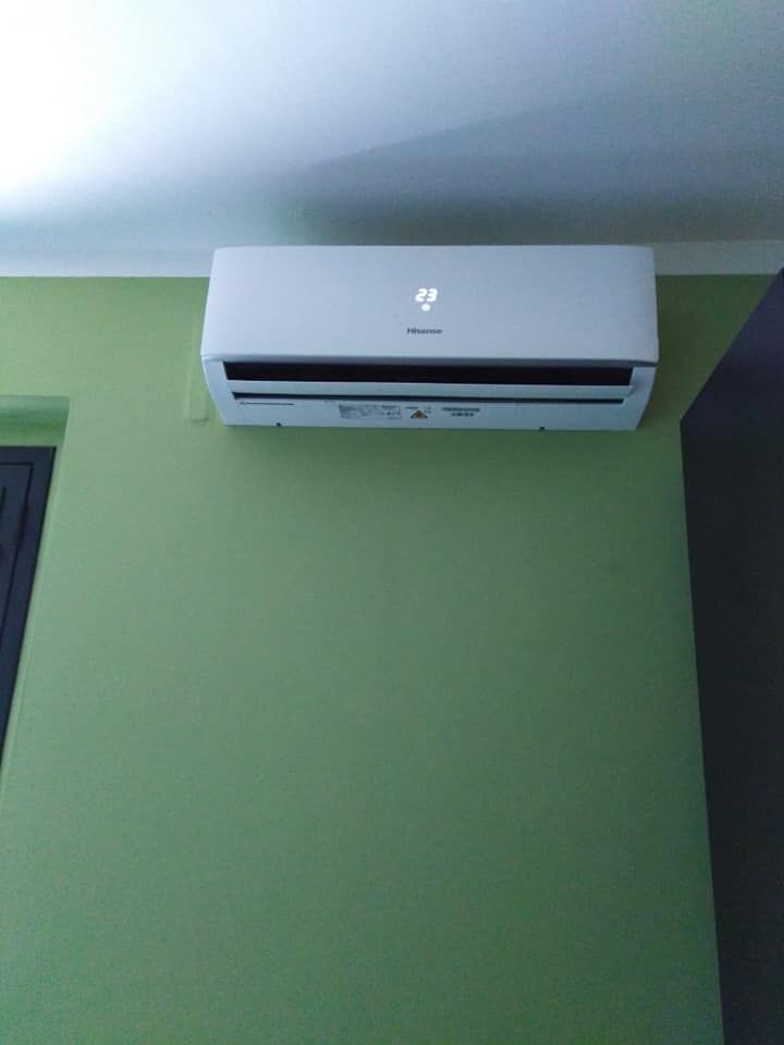 Condizionatore d'aria bianco a parete, installato su una parete verde vicino al soffitto.