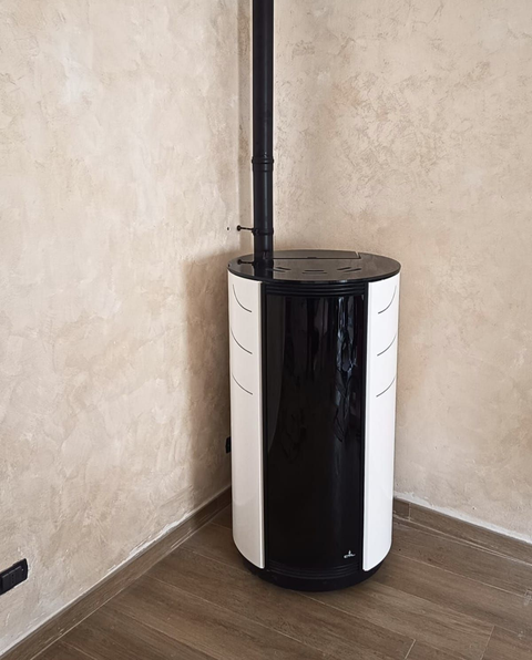 Stufa a pellet bianca e nera con tubo di ventilazione verticale in un angolo su pavimento in legno.