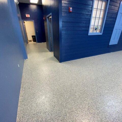 Blue hallway with speckled gray floor, open doorway, and windows on the right.