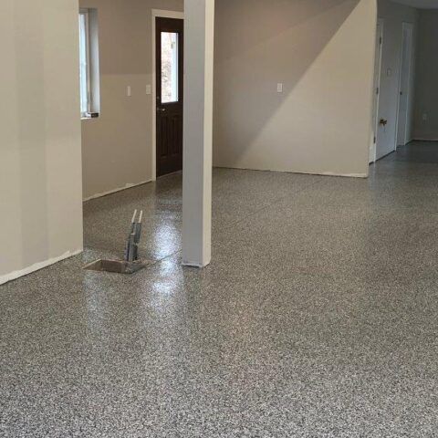 Empty unfinished room with speckled gray floor, beige walls, and a support column in the center