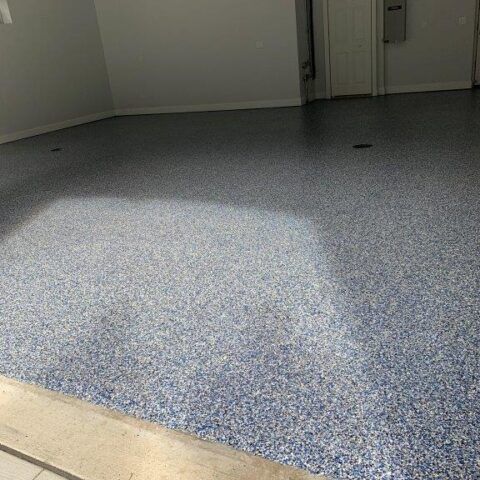Empty speckled garage floor with sunlight patch and closed doors in the background