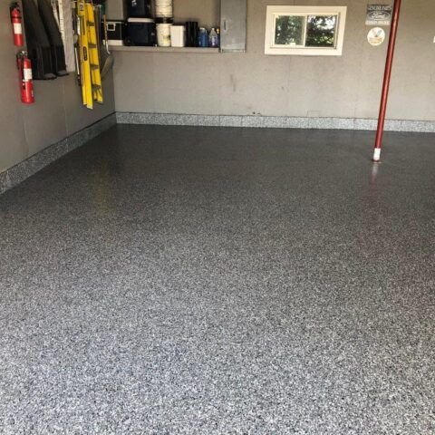 Empty garage with a gray speckled epoxy floor and wall-mounted storage shelves.