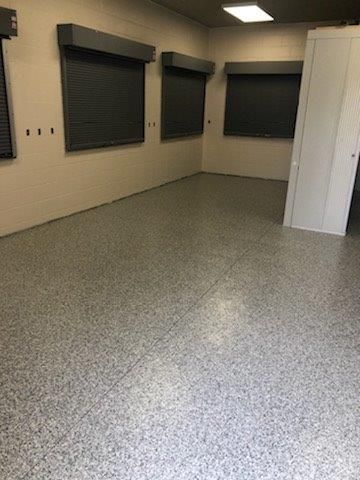 Empty room with speckled gray floor, beige walls, and dark window blinds.