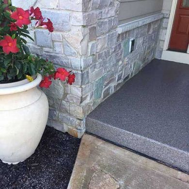 Front porch with stone siding, red door, concrete step, and large white planter with red flowers.
