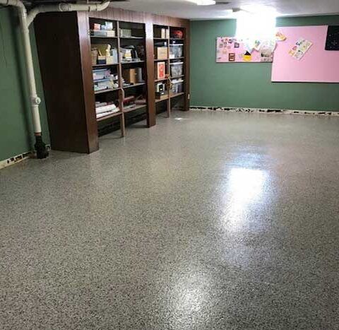 Empty basement room with polished speckled floor, shelves, and pink bulletin boards on green walls.