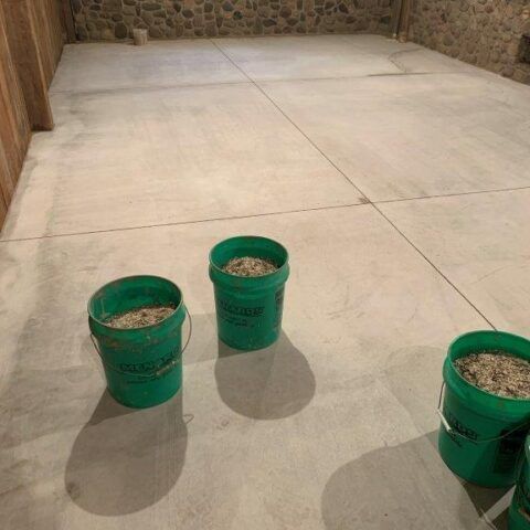 Three green buckets on a concrete floor in a stone-walled room
