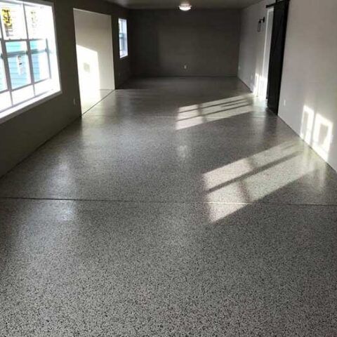 Empty sunlit room with gray speckled floor and long window shadows across the walls and floor