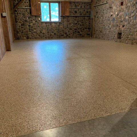 Empty stone-walled room with a speckled epoxy floor and a small window.