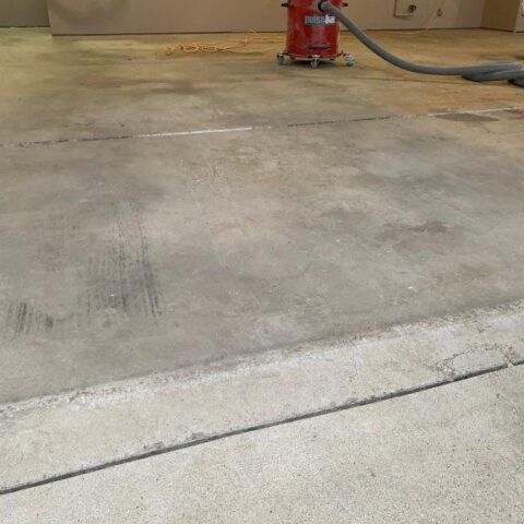 Empty concrete floor in a workshop, with a red tool and hose in the background.