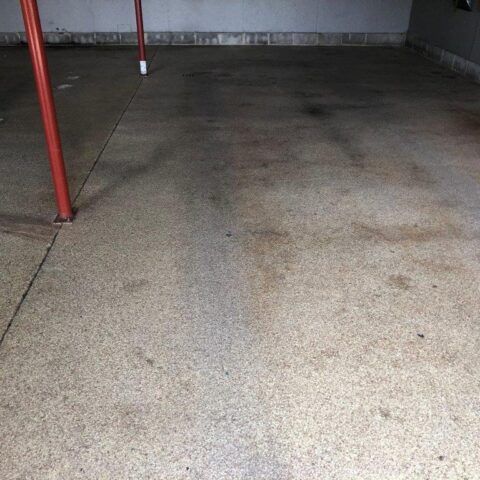 Empty concrete garage floor with red support posts and gray walls in the background
