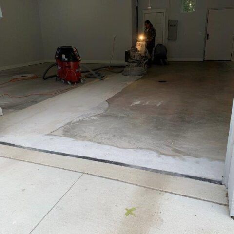 Partially renovated room with floor sander, vacuum, and a person working near the back wall.