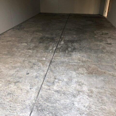 Empty concrete floor inside a narrow room, with a visible center seam and dim walls.