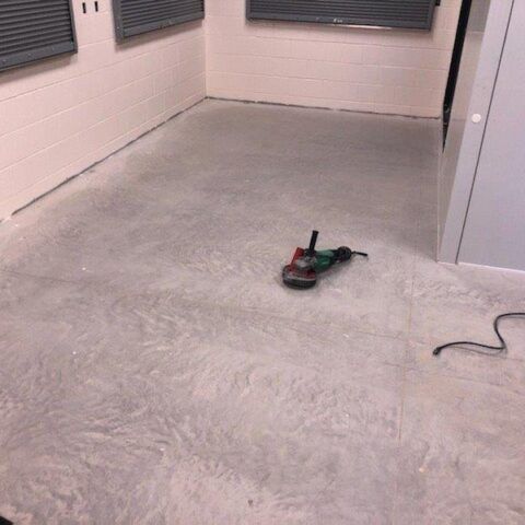Empty room with a newly sanded concrete floor and a floor grinder on the ground