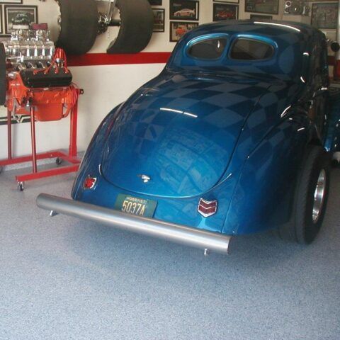 Blue vintage drag-style car in a garage, rear view with chrome bumper and large rear tires