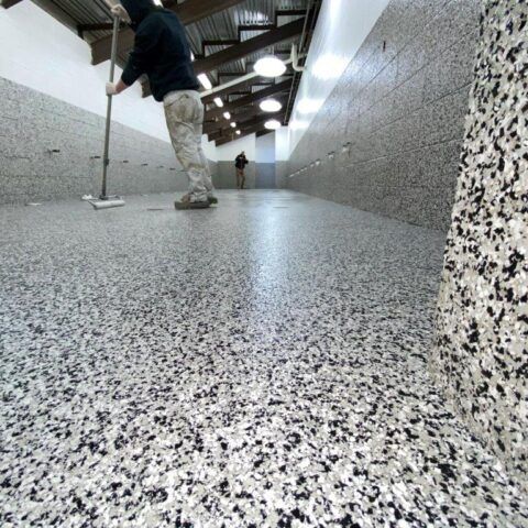 Person mopping a speckled hallway floor in a long indoor corridor.