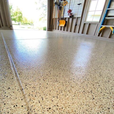 Speckled epoxy garage floor with open doorway and tools on the wall