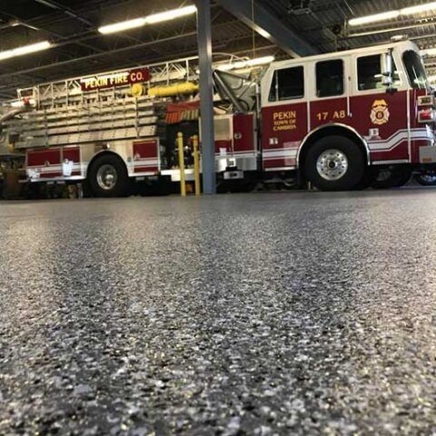 Red fire truck parked inside a fire station, seen from a low angle on a shiny floor.
