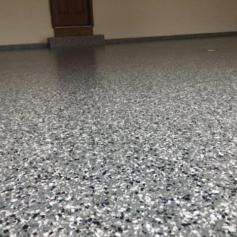Gray speckled floor in an empty indoor room with a beige wall and doorway in the background
