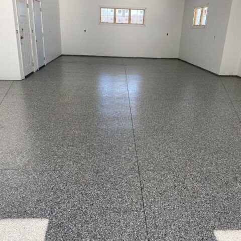 Empty gray room with speckled floor, white walls, and small windows at the far end