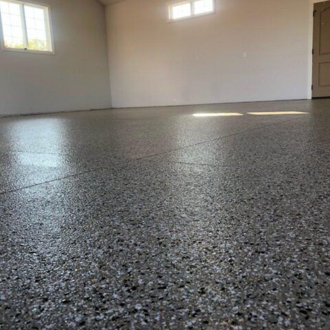 Empty speckled gray garage floor in a bright room with white walls and windows.
