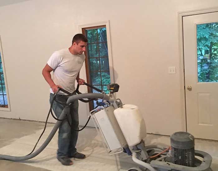 Man using a floor polishing machine on a room’s unfinished floor, with a dust hose attached