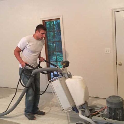 Man using a floor polishing machine in an unfinished room with white walls and a window