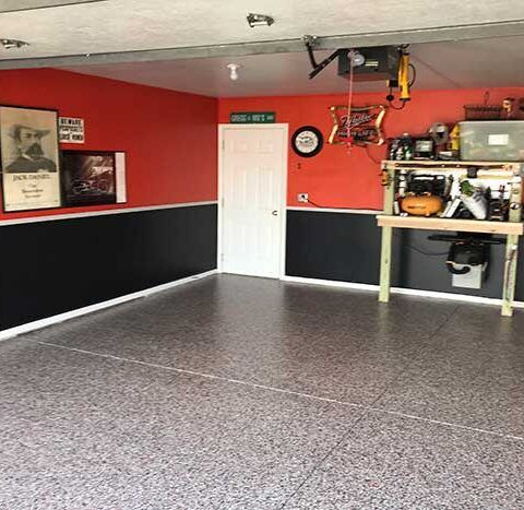Empty garage with red walls, black lower trim, gray floor, and storage shelves on the right.