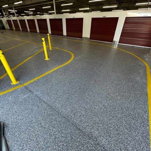 Indoor parking garage with gray concrete finished floor, yellow lane markings, and maroon storage unit doors