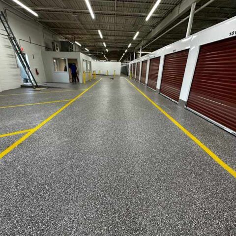 Wide indoor storage corridor with red roll-up doors, yellow floor lines, and a person in the distance
