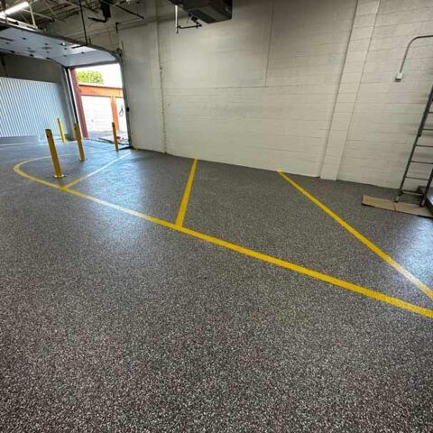 Empty warehouse with gray speckled floor, yellow parking lines, and an open doorway on the left.