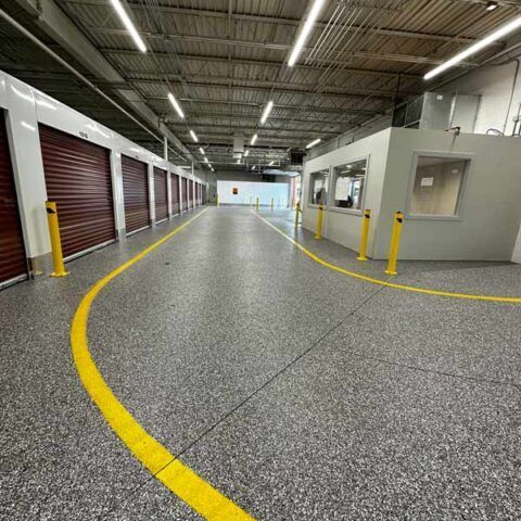 Empty warehouse aisle with yellow floor lines, storage units on the left, and an office booth on the right.