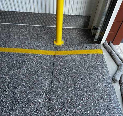 Yellow safety pole on speckled gray floor with a yellow line near a doorway