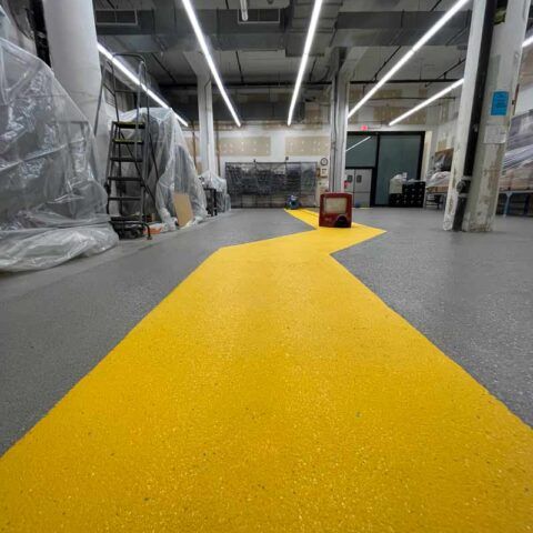 Indoor warehouse aisle with a bright yellow floor path leading toward equipment and storage shelves