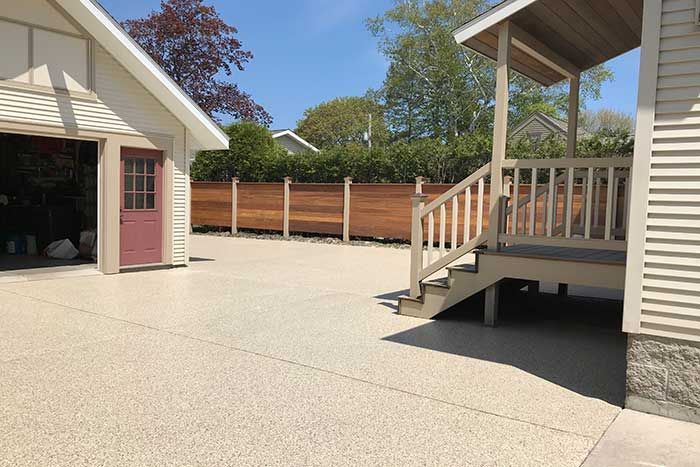 Backyard patio with beige house siding, stairs, and a wooden fence under a clear sky