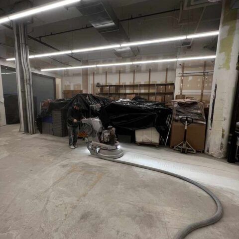 Industrial room with a floor buffer machine and a coiled hose on a concrete floor, surrounded by tarped equipment.