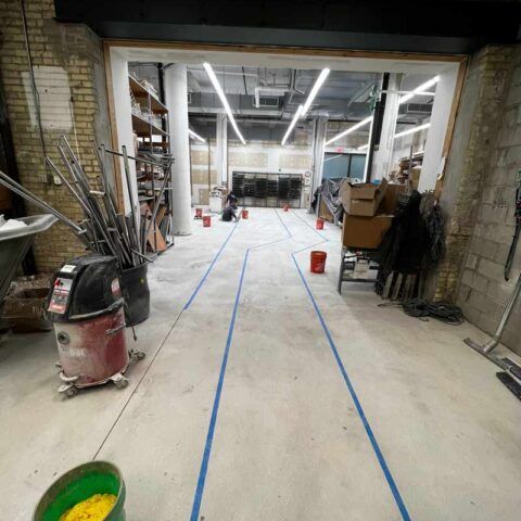 Industrial workshop under renovation with tools and supplies scattered along a long, taped floor path.
