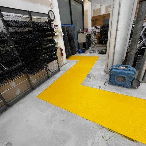 Indoor workshop with a bright yellow painted floor path, storage racks, and a blue machine on the right