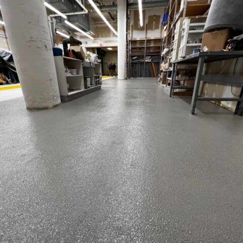 Low-angle view of a warehouse aisle with gray epoxy floor, shelves, and storage bins.