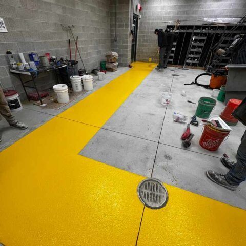 Construction floor with bright yellow epoxy walkway and a floor drain in a utility room.