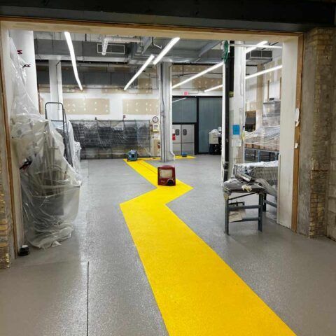 Industrial workspace with a bright yellow zigzag path on a gray floor and equipment along the sides