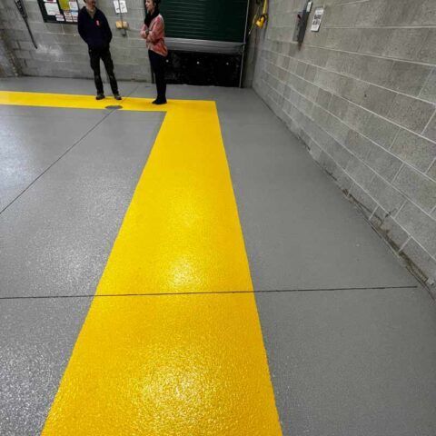 Yellow tactile path leading through a subway corridor, with two people standing near a doorway at the end.