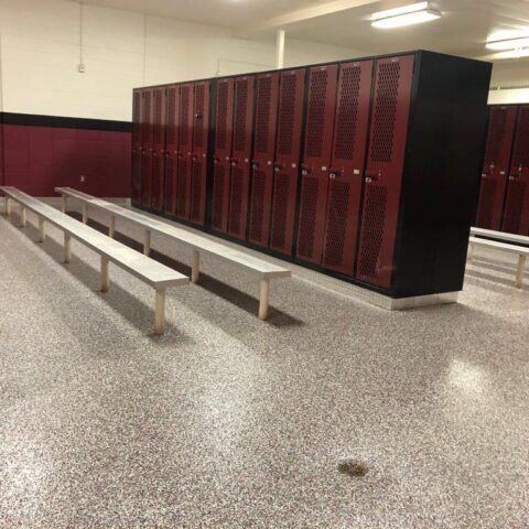 Empty school locker room with maroon lockers, white benches, and speckled floor