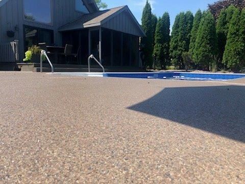 Low-angle view of a backyard pool deck beside a modern house and tall hedges