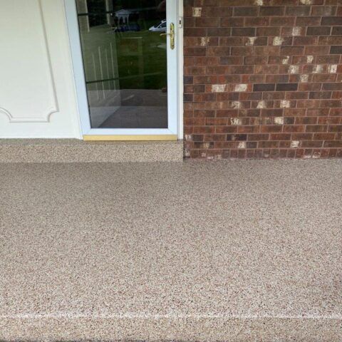 Brick porch with speckled concrete floor and glass front door beside a white door panel.