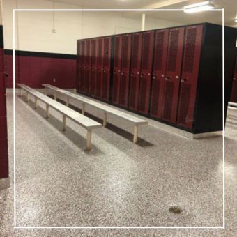 Empty school locker room with maroon lockers, gray benches, and speckled flooring